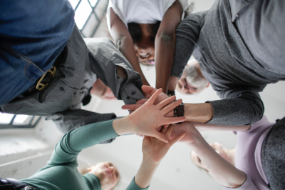 hands This image shows a group of people standing in a circle with their hands stacked together in the center. The perspective is from below, looking up.