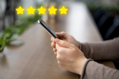 stars The image shows a person holding a smartphone. Above the phone, there are five yellow stars (five-star rating).